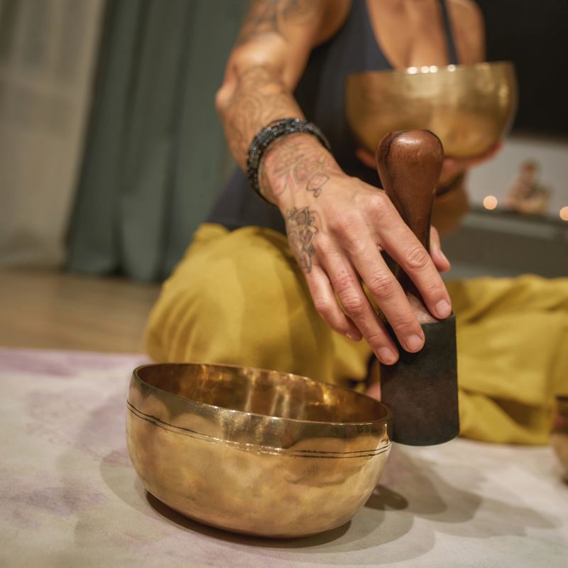 Young woman playing singing bowl while sitting on floor at home, selective focus, cropped. Yoga concept, meditation and sound therapy