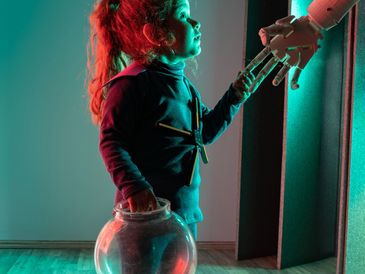 A young girl holding a fishbowl and touching a robotic hand.