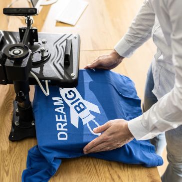 Person flattening a blue 'Dream Big' t-shirt on a wooden table.