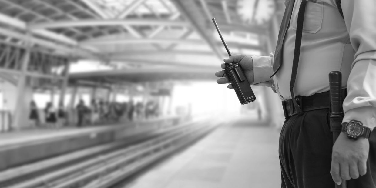 Security guard holding a walkie-talkie at a train station platform.