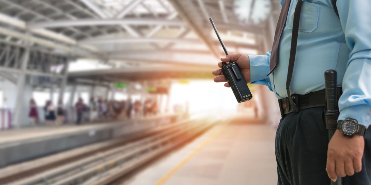 Security guard holding a walkie-talkie at a train station platform.