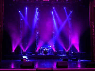 Empty stage with vibrant purple and blue lighting focused on a drum set.