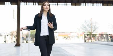 Businesswoman with suitcase and phone outdoors.