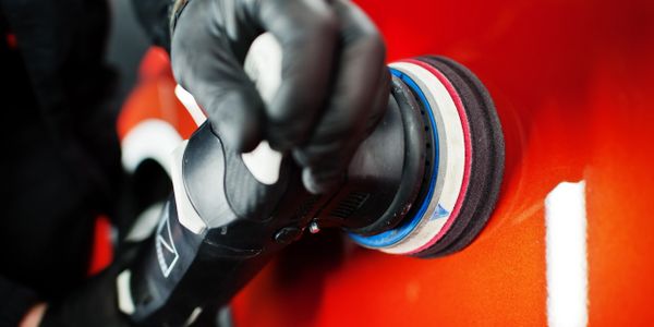 Person polishing a shiny red car with a rotary buffer.
