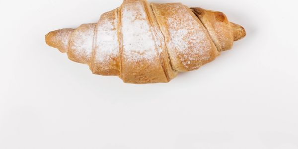 Fresh croissant dusted with powdered sugar on a white background.