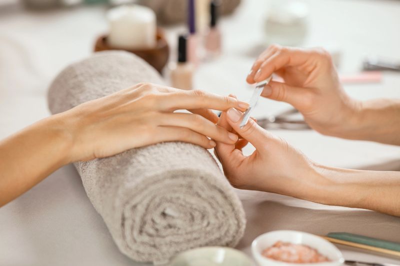 Close up shot of a woman in a nail salon receiving manicure by beautician with metal nail file. Woman getting nail manicure at spa centre. Beautician file nails to a customer in luxury salon.