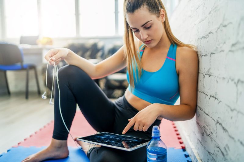 Beautiful sporty woman resting, listening to music and using digital tablet after workout