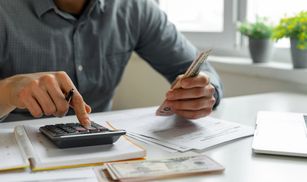 Person calculating finances using a calculator and bills.