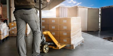 Worker moving pallet of boxes with pallet jack.