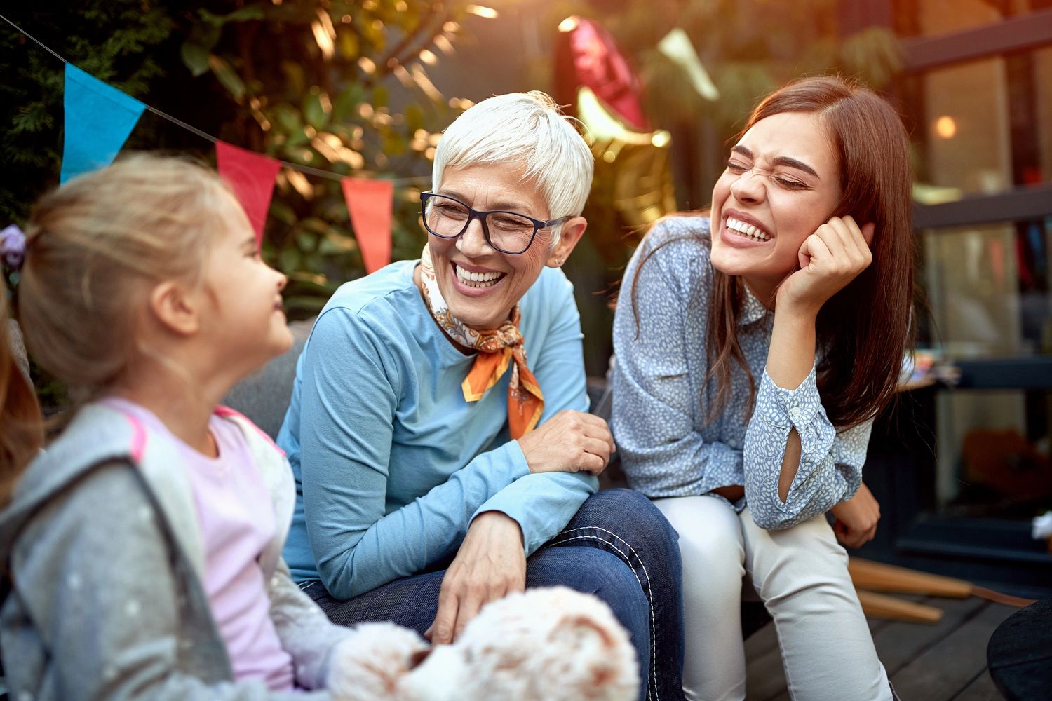 Three generations of women laughing together outdoors at a celebration.