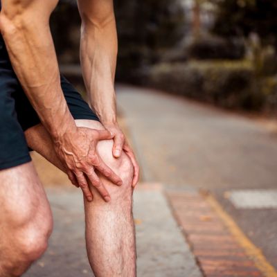 Person holding their knee in pain outdoors.