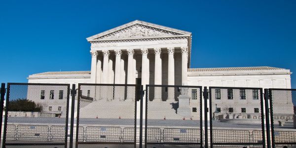 The U.S. Supreme Court building behind a tall security fence on a clear day.