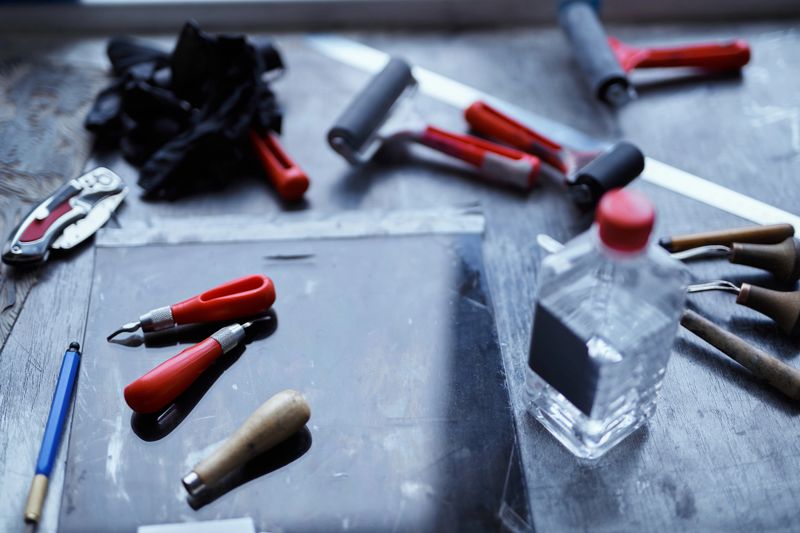 Linocut concept. Working tools in red and black colors on dark table. Cutting instruments, ink roller and other tools for linocut making. High quality photo