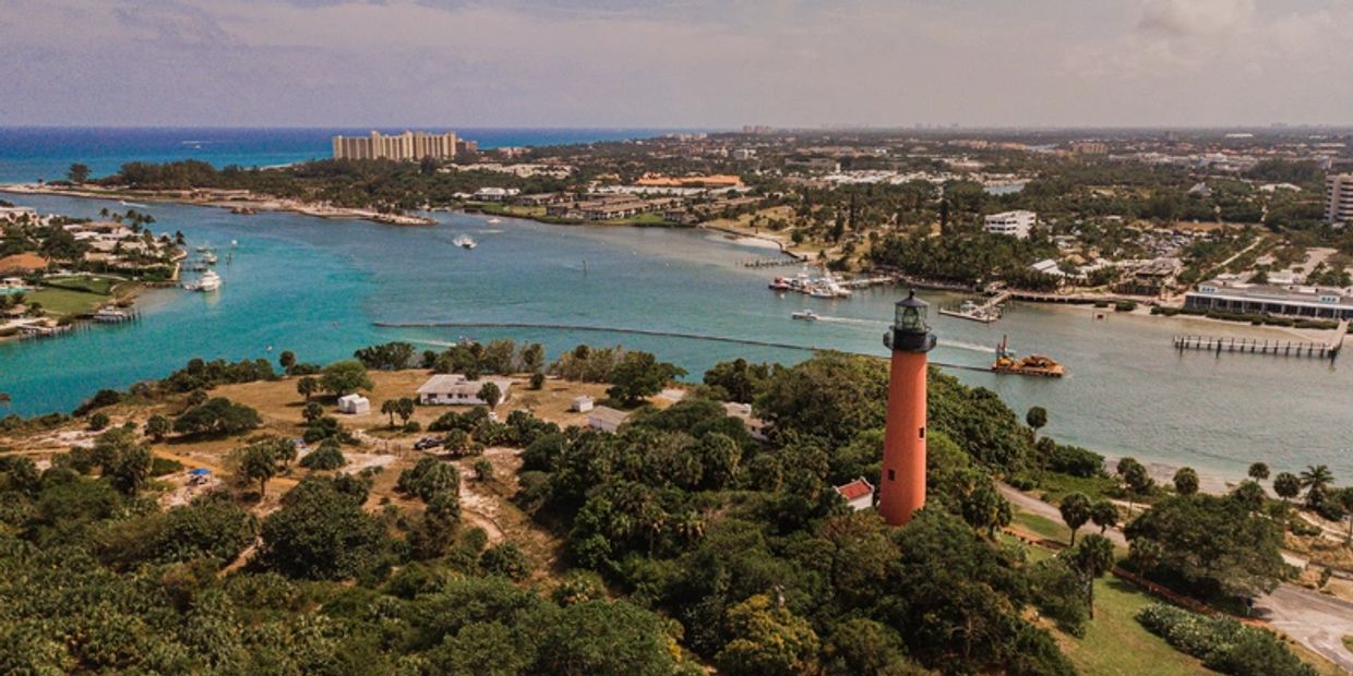 Scenic aerial view of a lighthouse by the water with surrounding greenery and boats.
