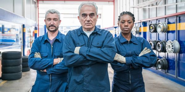 Three confident mechanics standing with arms crossed in a garage.