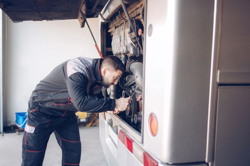 Male mechanic working on repairing a bus engine at service garage.