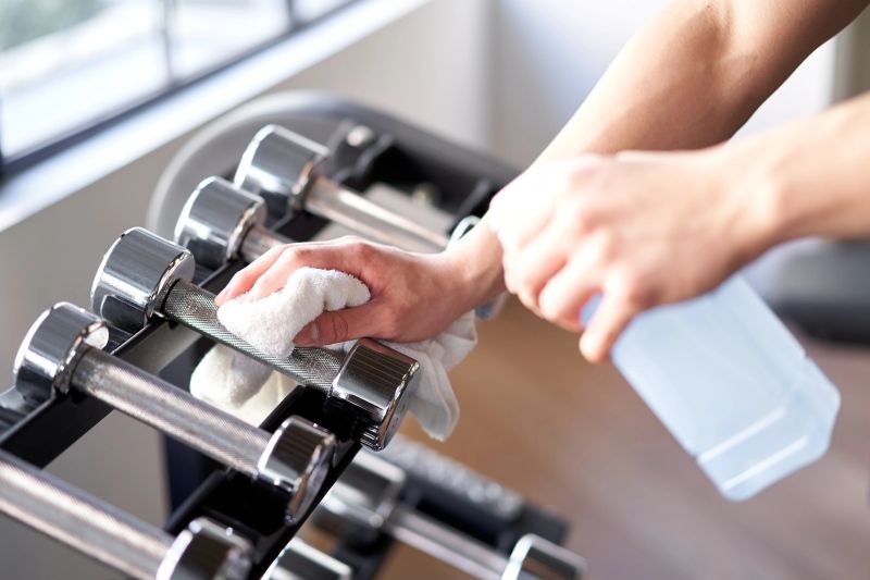 Hands of an Asian male trainer sterilizing dumbbells in a training gym