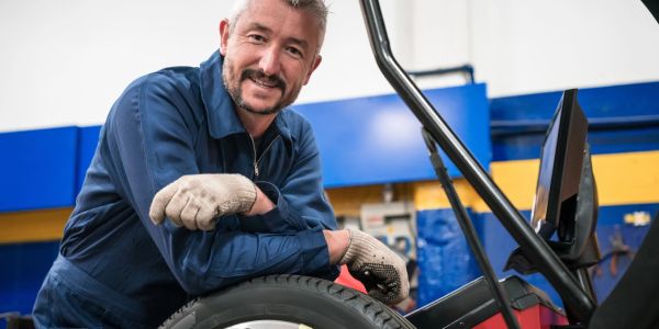 Smiling mechanic leaning on a car tire in a workshop.
