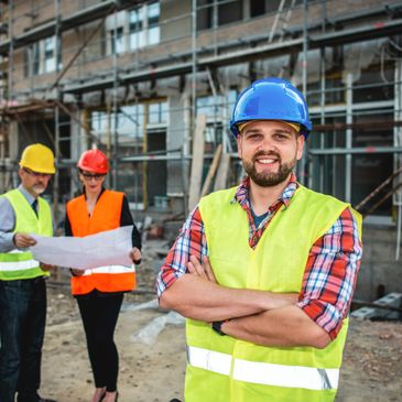Construction workers in safety gear at a building site, with one smiling confidently.