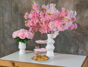 Elegant pink flowers in white vases with pastries on a wooden table.
