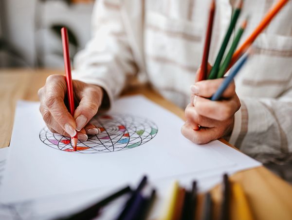 Person coloring a geometric pattern with colored pencils.