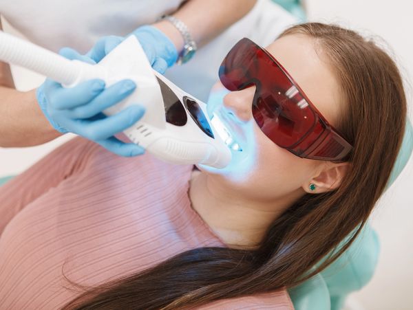 Woman wearing protective glasses getting teeth whitening treatment with blue light.