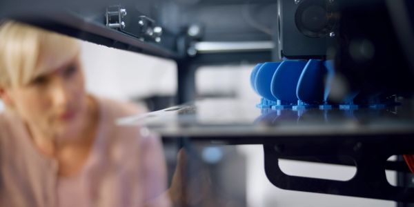 Woman observing blue objects being 3D printed.
