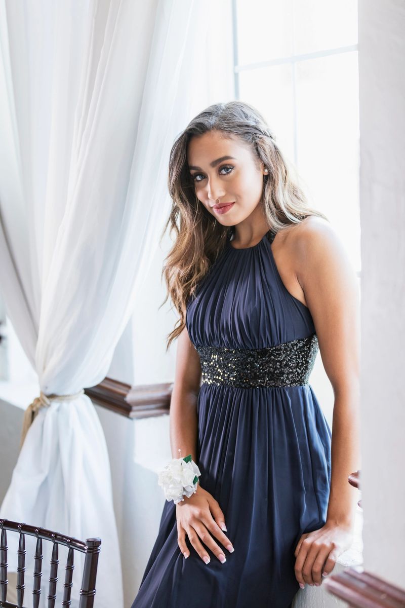 A mixed race teenage girl, 16 years old, standing by a window, wearing a prom dress and wrist corsage.