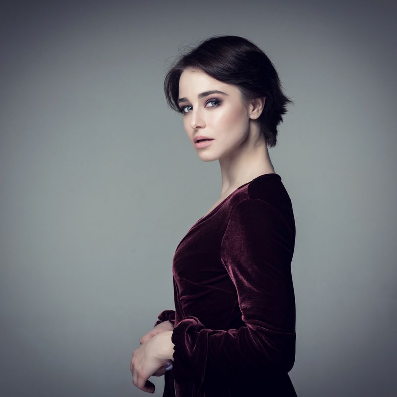 Beauty female portrait. Young attractive woman posing at studio over gray background. Beautiful model with perfect make-up dressed evening burgundy dress looking at camera. Professional studio photo.