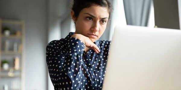 Woman in a polka dot shirt looking thoughtfully at a laptop.