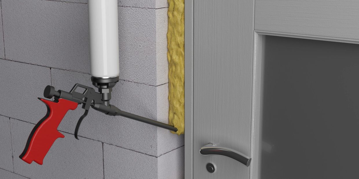 Expanding foam gun sealing gap around door frame for insulation.