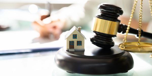 A gavel, scales of justice, and a small house model on a desk.