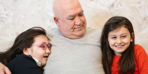 Grandfather warmly embraces two smiling granddaughters on a cozy couch.