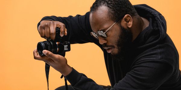 Man focusing while holding a camera against an orange background.