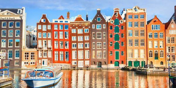 Scenic view of Amsterdam’s historic canals lined with traditional Dutch houses, bicycles, and boats under a clear sky, showcasing the city’s charming waterfront and iconic architecture.