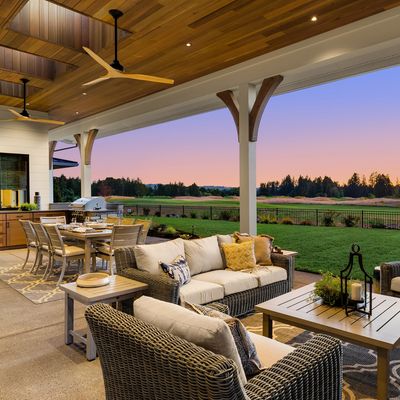 Covered outdoor patio with cozy wicker furniture and dining area overlooking a grassy landscape at sunset.
