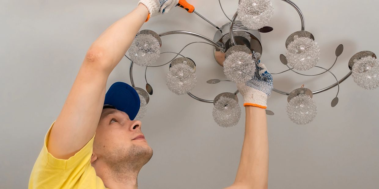 Man fixing chandelier with screwdriver and gloves.