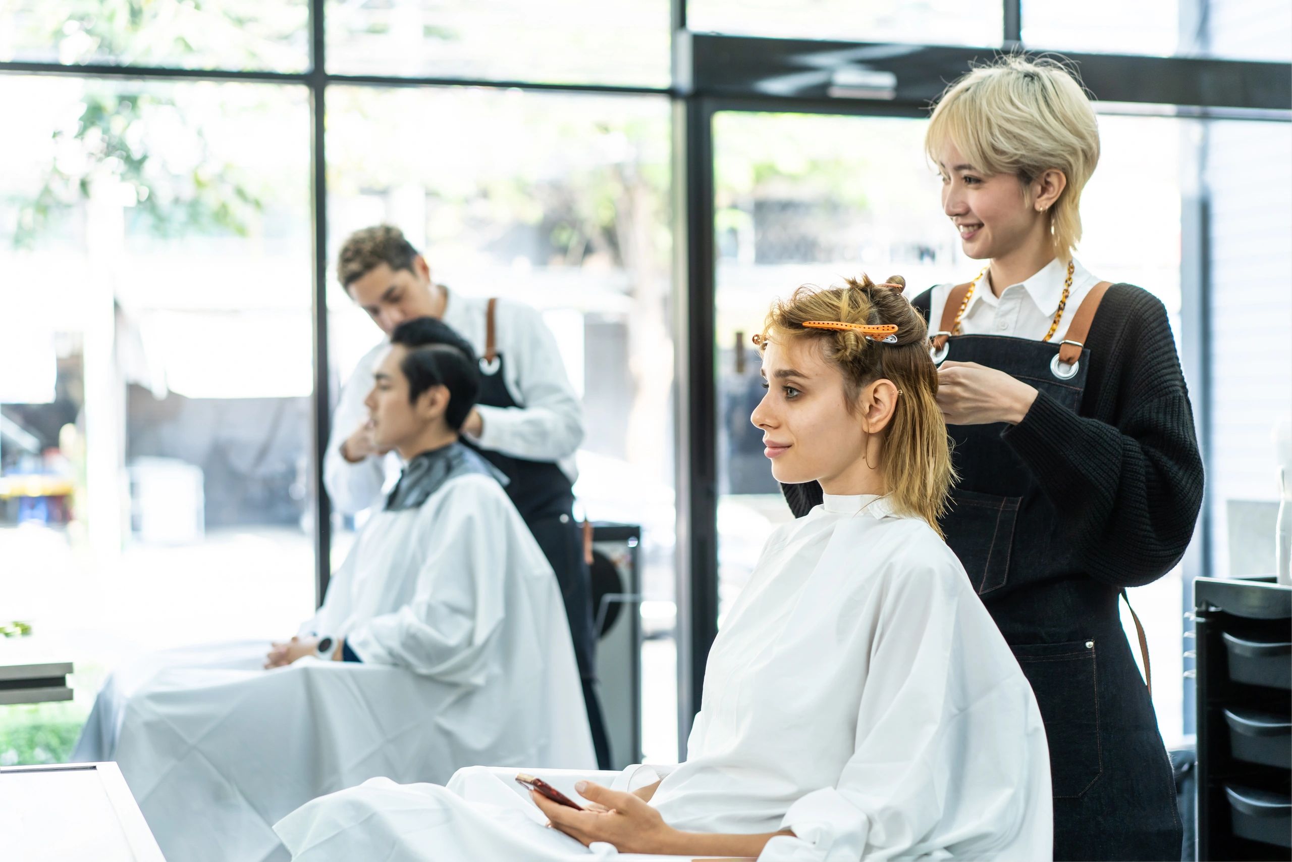 Hairdressers cutting clients' hair in a bright salon.