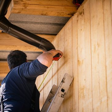 A man measuring wooden wall while standing on a ladder.
