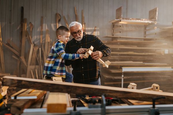Grandfather and grandson building a wooden airplane in a workshop.