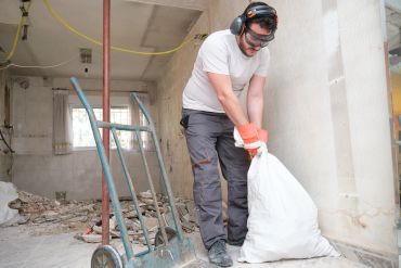 Worker in protective gear lifting a heavy bag in a construction site.