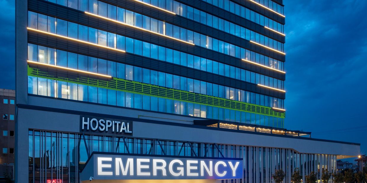 Modern hospital building with illuminated emergency sign at dusk.