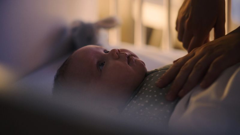 Authentic Close Up Shot of a Mother Soothing and Holding Hand of a Newborn Baby in Child Crib. Caucasian Neonate Toddler at Home in Kids Bedroom. Concept of Childhood, New Llife and Parenthood.