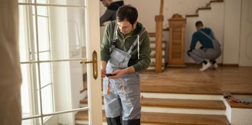Two men renovating a house, one measuring a door frame.