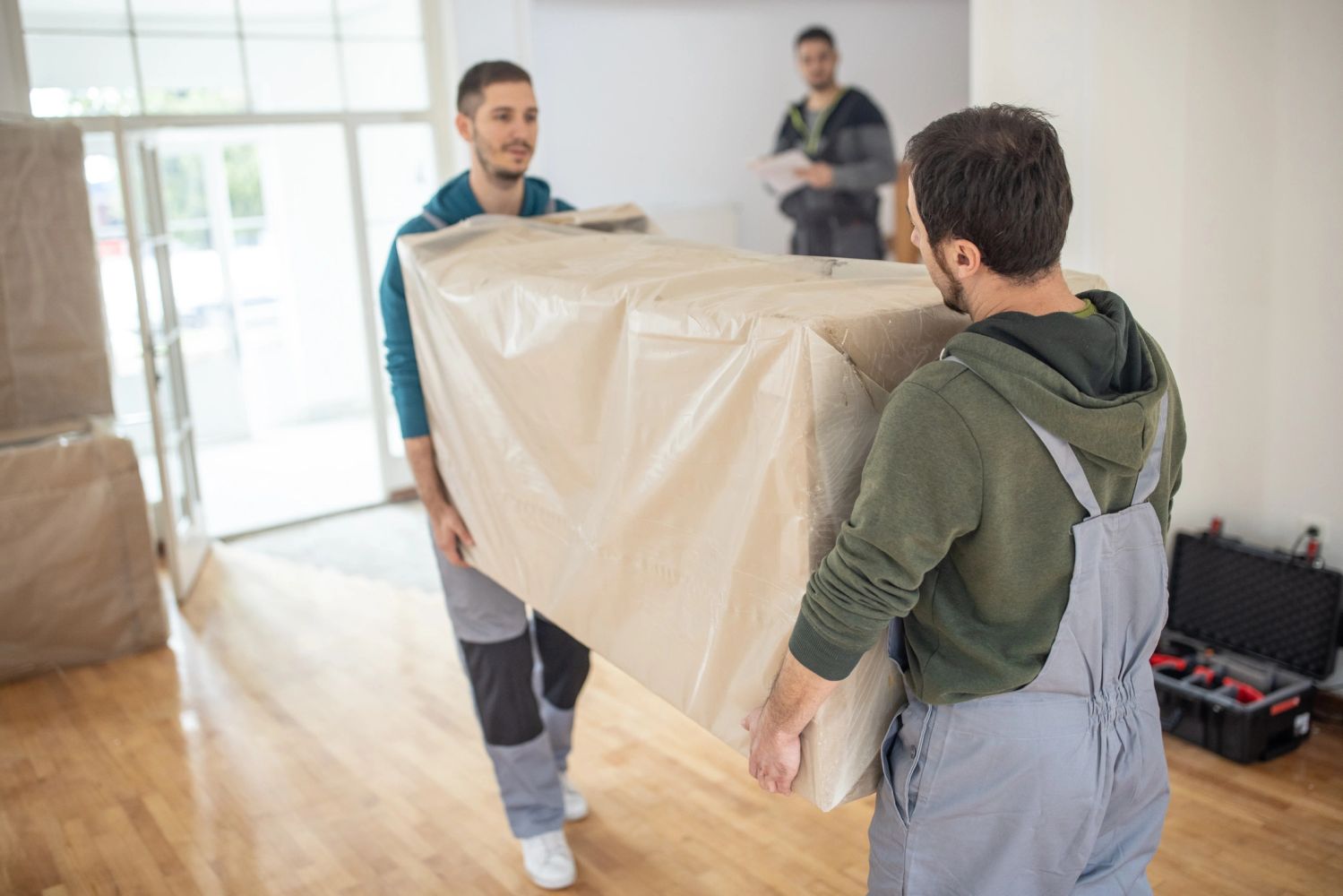 Two men carrying a large wrapped box in a bright room.