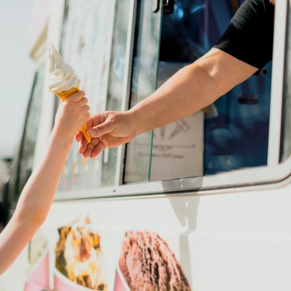Hand passing an ice cream cone to a child from a truck.