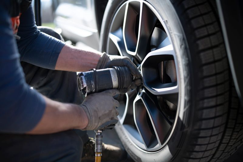 Close-up shot of an unrecognizable auto repairman changing whleel and tire in a workshop.