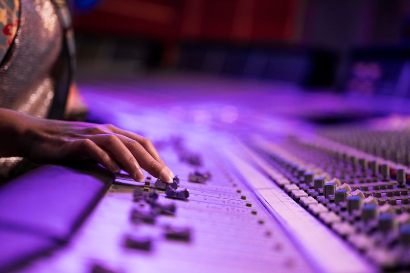 Close-up of female fingers fine tuning sound by moving faders on mixing control panel. Selective focus. Music, arts and entertainment concept.