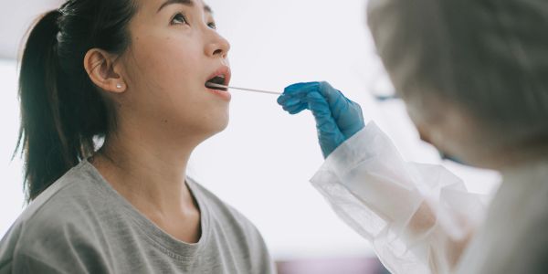 Healthcare worker takes a throat swab from a woman for testing.