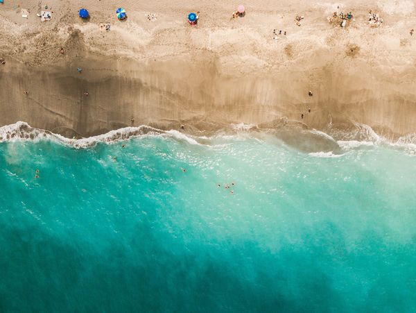 Aerial view of a beach with umbrellas and people near turquoise water.